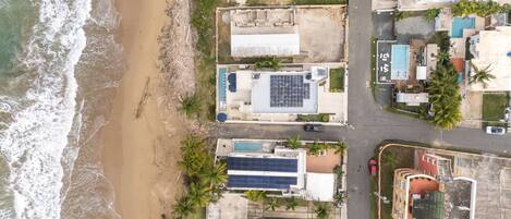 An aerial view of a coastal property with a beach, solar panels, and a swimming pool.