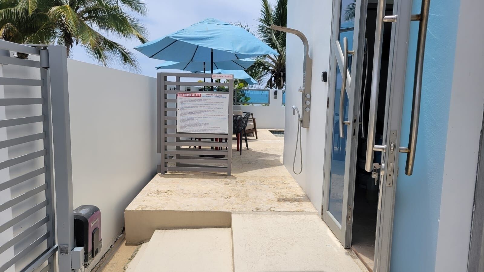 A gated entrance to a building with a blue umbrella and a signboard.
