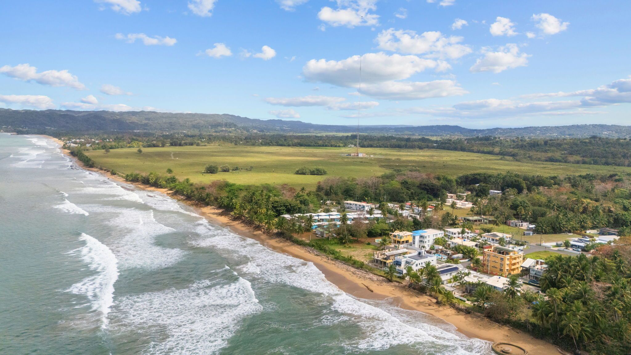 Une zone côtière comprenant une plage, des immeubles résidentiels et une chaîne de montagnes visible au loin.
