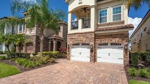 A two-story house with a stone facade, a balcony, and two garage doors.