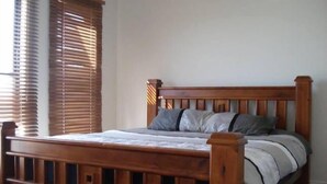 A wooden bed with a headboard, a window with blinds, and a plain wall. - Bunker Vista at Dunes Golf Links (Port Hughes)