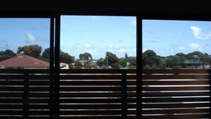A view through a window with horizontal blinds, featuring a residential area with houses and trees. - Bunker Vista at Dunes Golf Links (Port Hughes)