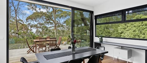 A modern dining area with a large table, chairs, and a view of the outdoors through large windows.