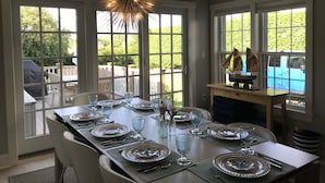 Een eetruimte met een grote tafel voor zes personen, grote ramen en een decoratieve lamp.