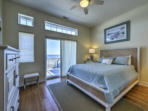 A bedroom with a large bed, a ceiling fan, a window with blinds, a bench, and a view of the outdoors. - Direct Beach Access and Expansive Atlantic Ocean Views! (North Wildwood)