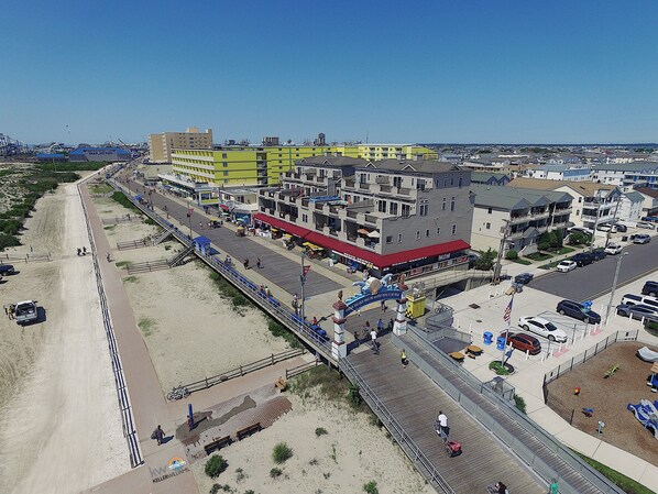 A coastal boardwalk with a beachside restaurant and a multi-story building with balconies. - Direct Beach Access and Expansive Atlantic Ocean Views! (North Wildwood)