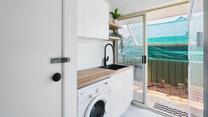 A compact laundry room with a washing machine, a sink, and a wooden countertop. - Busselton Family Holiday House - by the bay (Busselton)