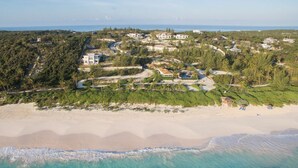 An aerial view of a coastal resort with multiple buildings, a sandy beach, and clear turquoise waters.