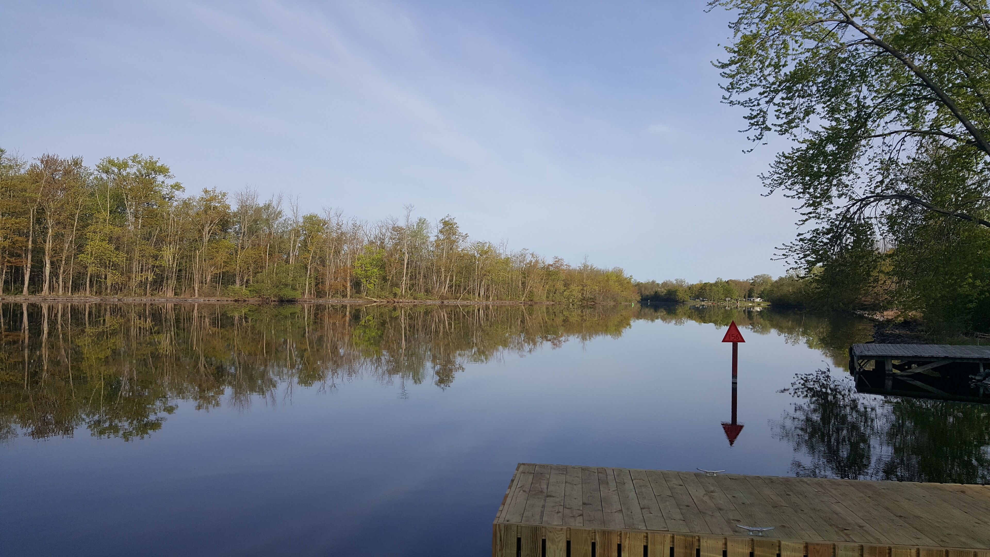 A calm lake with a wooden dock and a red directional sign.