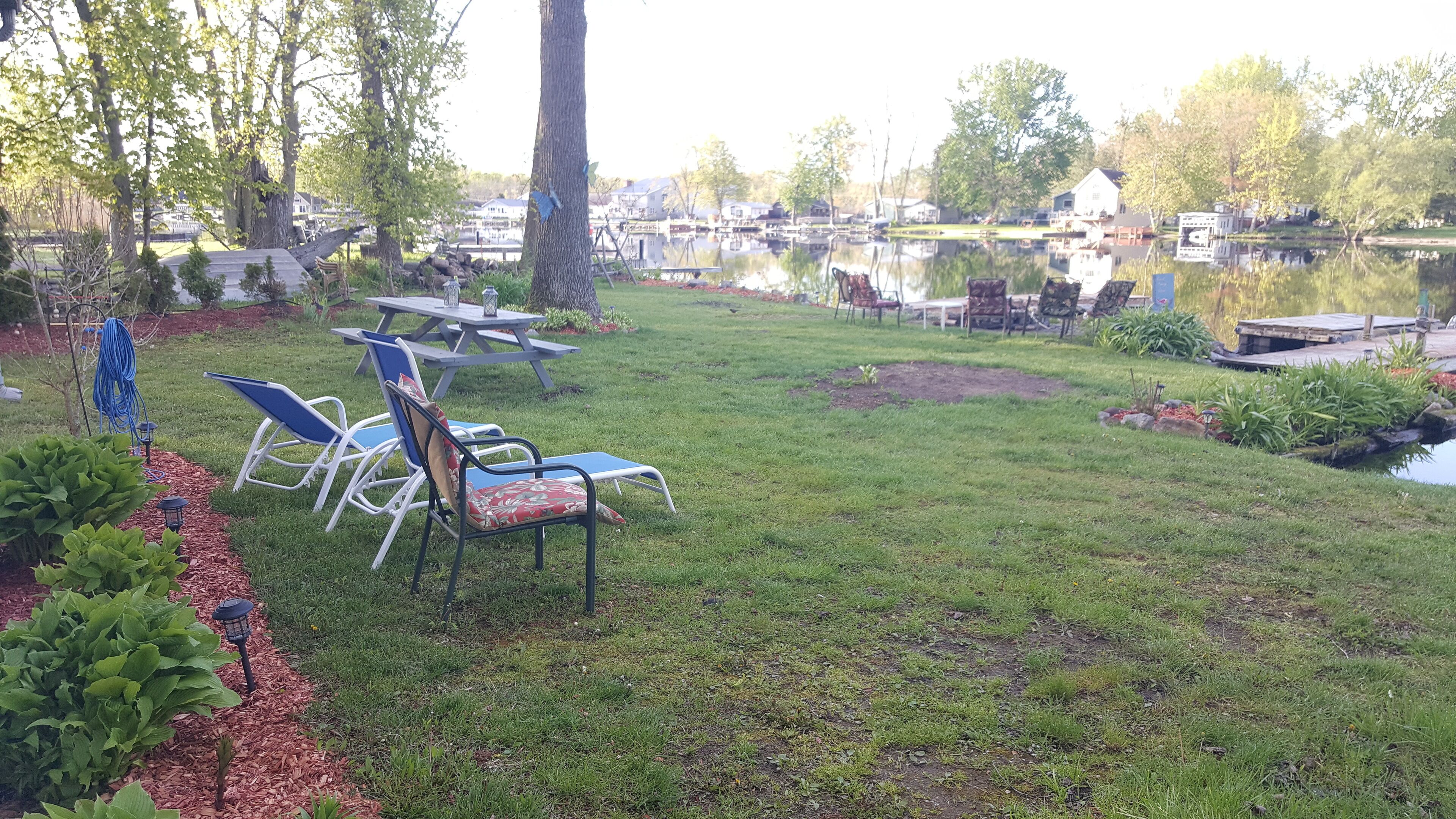 Un espacio al aire libre con césped, mesas y sillas de picnic, un pequeño estanque y un muelle.