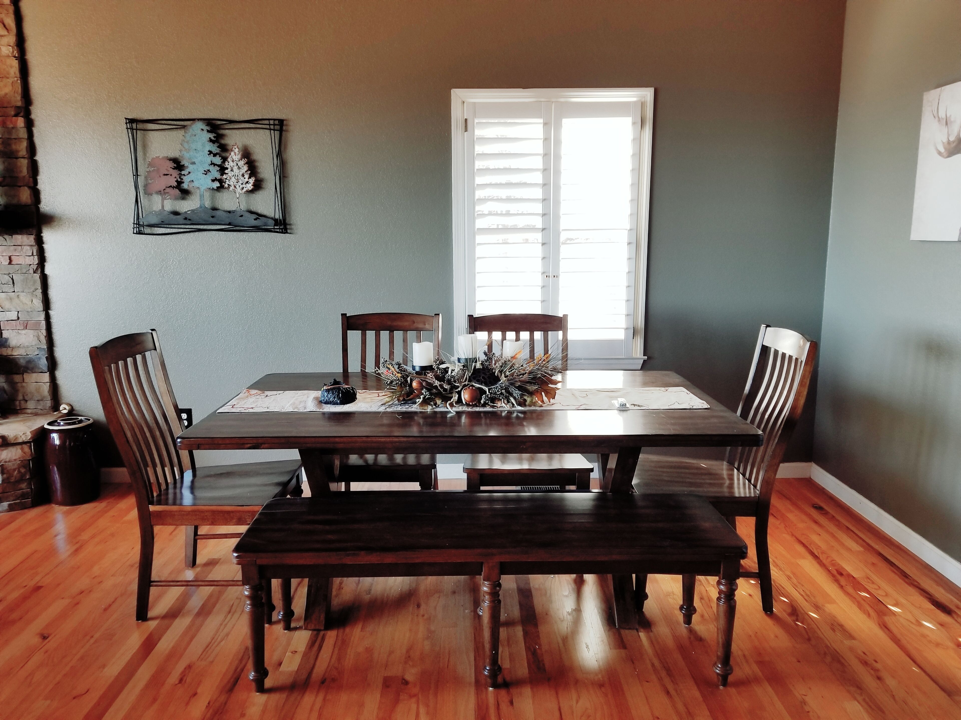 Comedor con mesa de madera, cuatro sillas, un banco, chimenea y ventana con persianas.