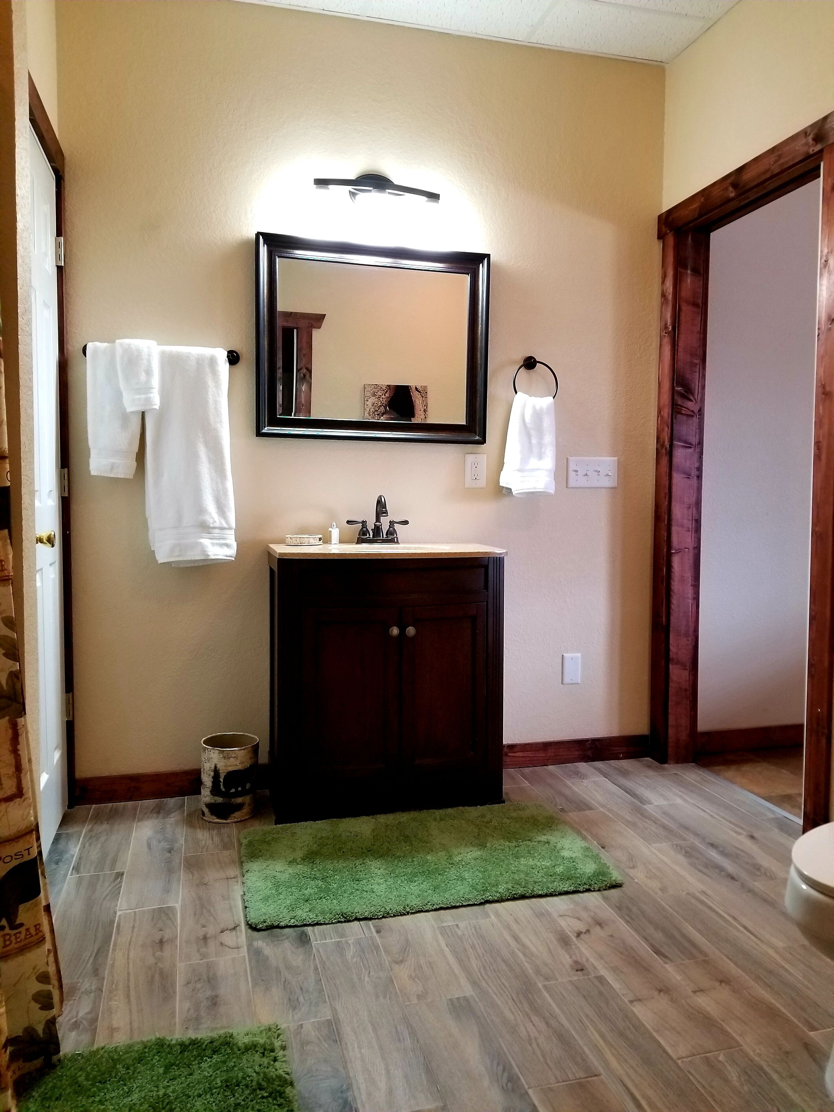 Un baño con un tocador de madera, un espejo y dos toallas blancas colgadas en la pared.