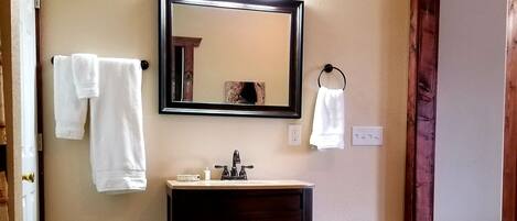 Un baño con un tocador de madera, un espejo y dos toallas blancas colgadas en la pared.