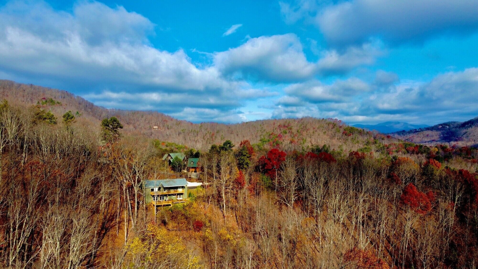 A two-story building with a green roof, surrounded by autumn-colored trees and hills in the background.