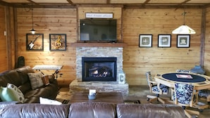 L’intérieur chaleureux d’un chalet avec une cheminée en pierre, des meubles en cuir et un téléviseur fixé au mur.