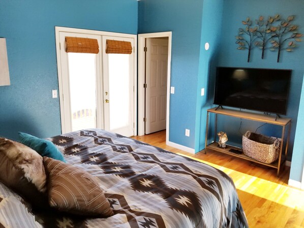 A bedroom with a bed, a TV on a stand, and a door with a window.