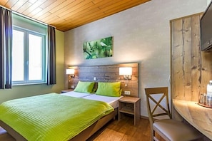 Une chambre d’hôtel comprenant un lit, deux tables de chevet, une chaise, une tête de lit en bois et un téléviseur fixé au mur.