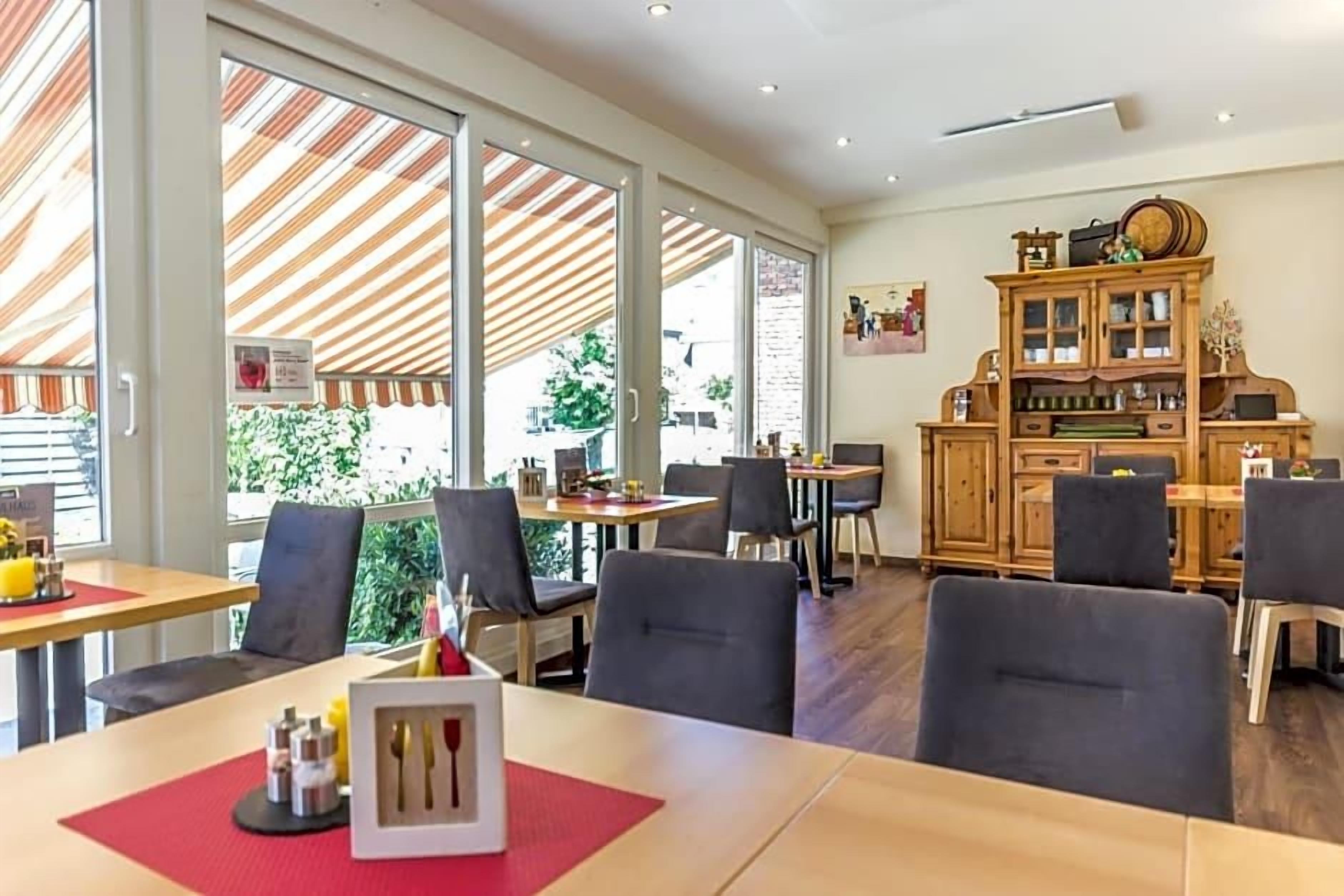 Een eetruimte met tafels en stoelen, een houten kast met glazen deuren en grote ramen voor natuurlijk licht.