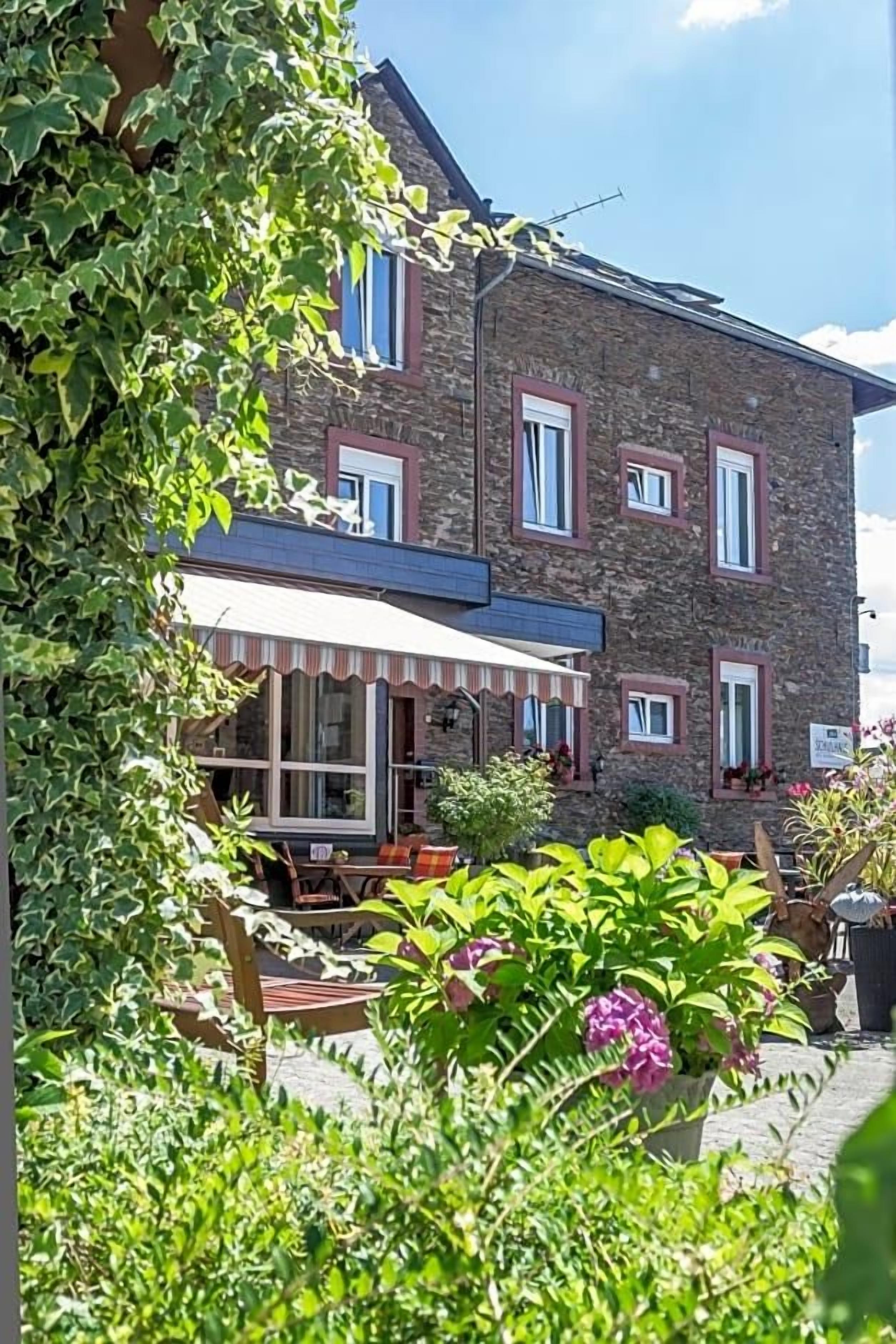 Een stenen gebouw met een overdekt terras en een tuin met diverse beplanting.