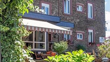 Een stenen gebouw met een overdekt terras en een tuin met diverse beplanting.