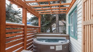 Ett område med en utomhusbubbelpool i trä, med en pergola ovanför, omgivet av snötäckta träd.