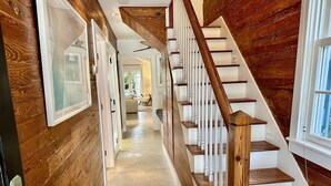 Un interior de madera con una escalera, un pasillo con cuadros enmarcados y vistas a una sala de estar.