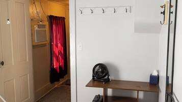 Une pièce avec un ventilateur de plafond, un lit, un banc avec une valise, un radiateur et un miroir au mur.