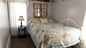 A bedroom with a bed, a nightstand, a lamp, a window with curtains, and a wall clock.