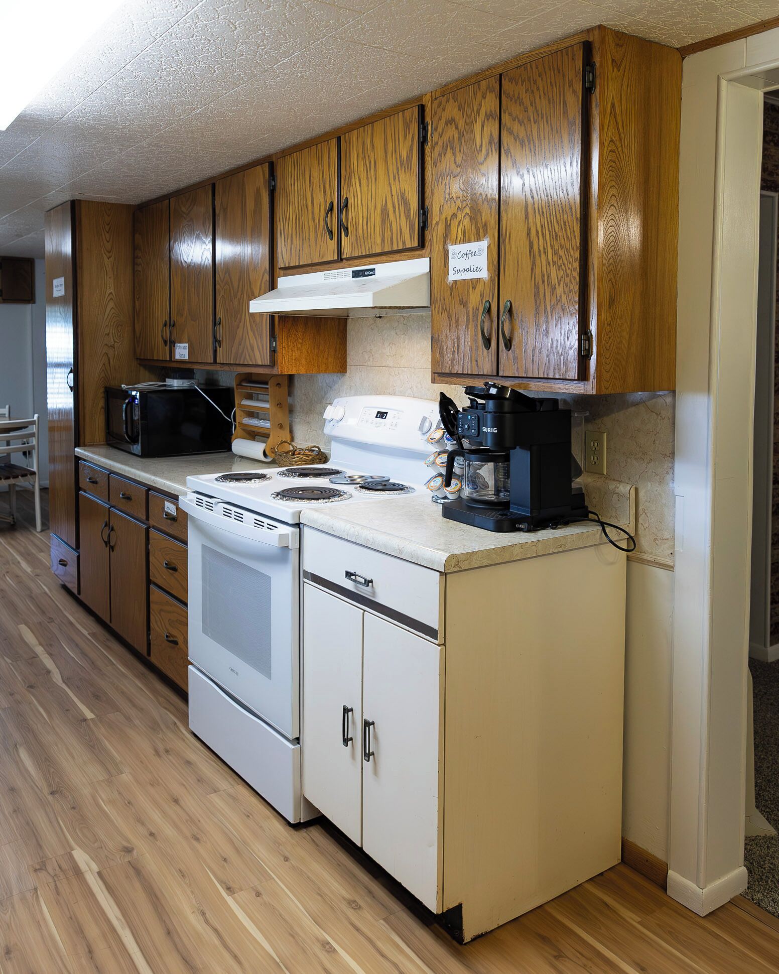 A compact kitchen with wooden cabinets, a microwave, a stove, and a coffee maker.