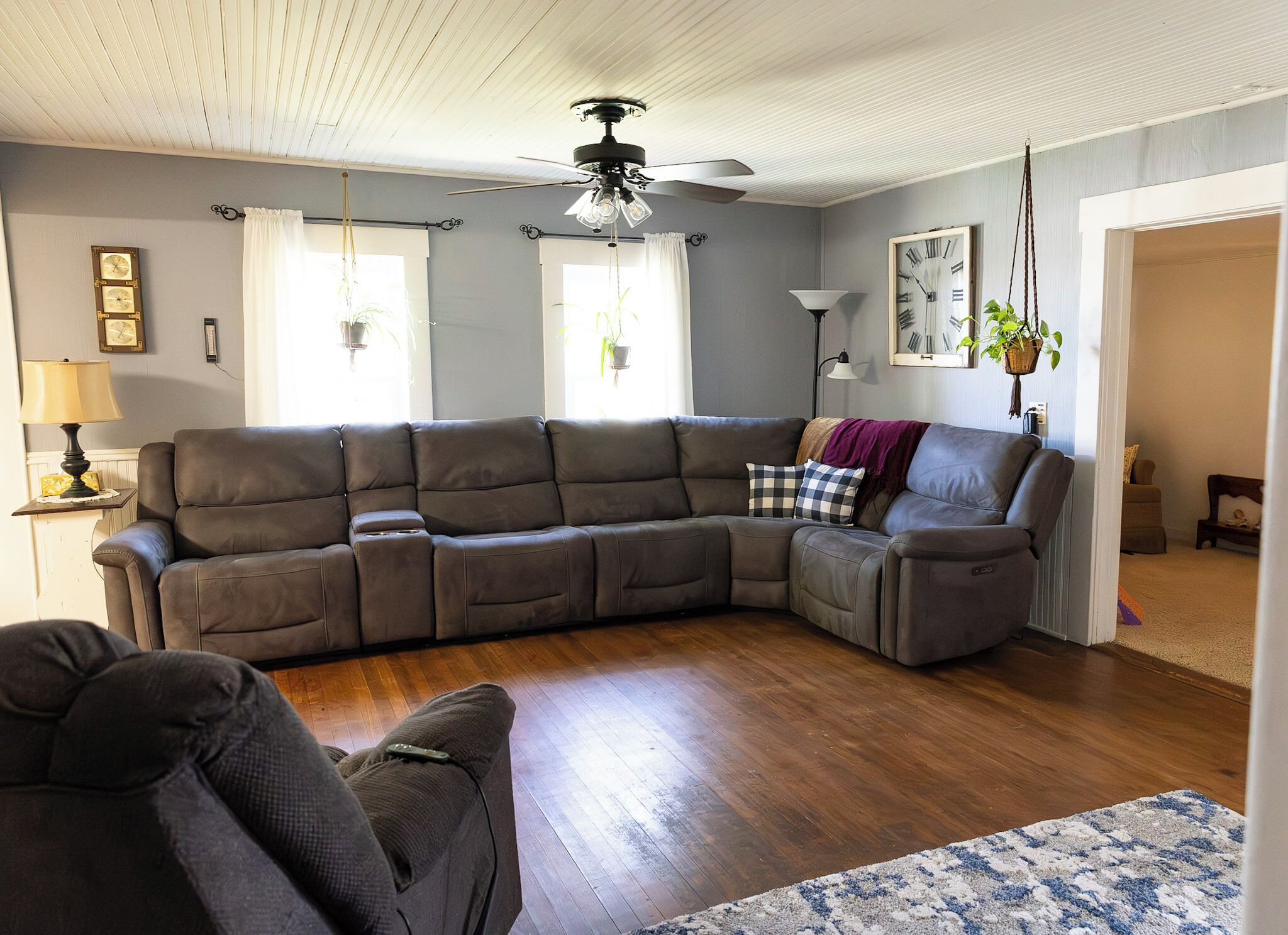 A living room with a sectional sofa, a ceiling fan, a clock, and a plant.