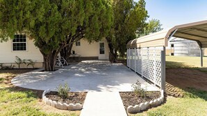 Propiedad residencial con patio cubierto, jardín cercado y una casa con ventana y puerta.
