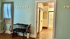 Una habitación con un banco de madera, una mesita, una planta en maceta y una puerta que da a otra habitación.