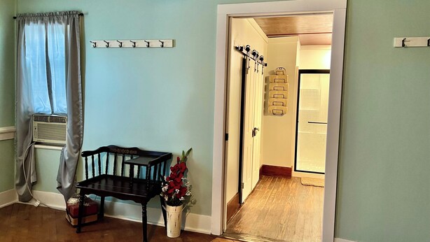 Una habitación con un banco de madera, una mesita, una planta en maceta y una puerta que da a otra habitación.