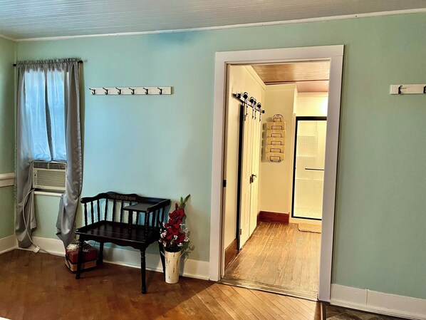 A room with a wooden bench, a small table, a potted plant, and a door leading to another room. - Country Farmhouse, family friendly, beautiful views, gorgeous sunsets (Thomas)
