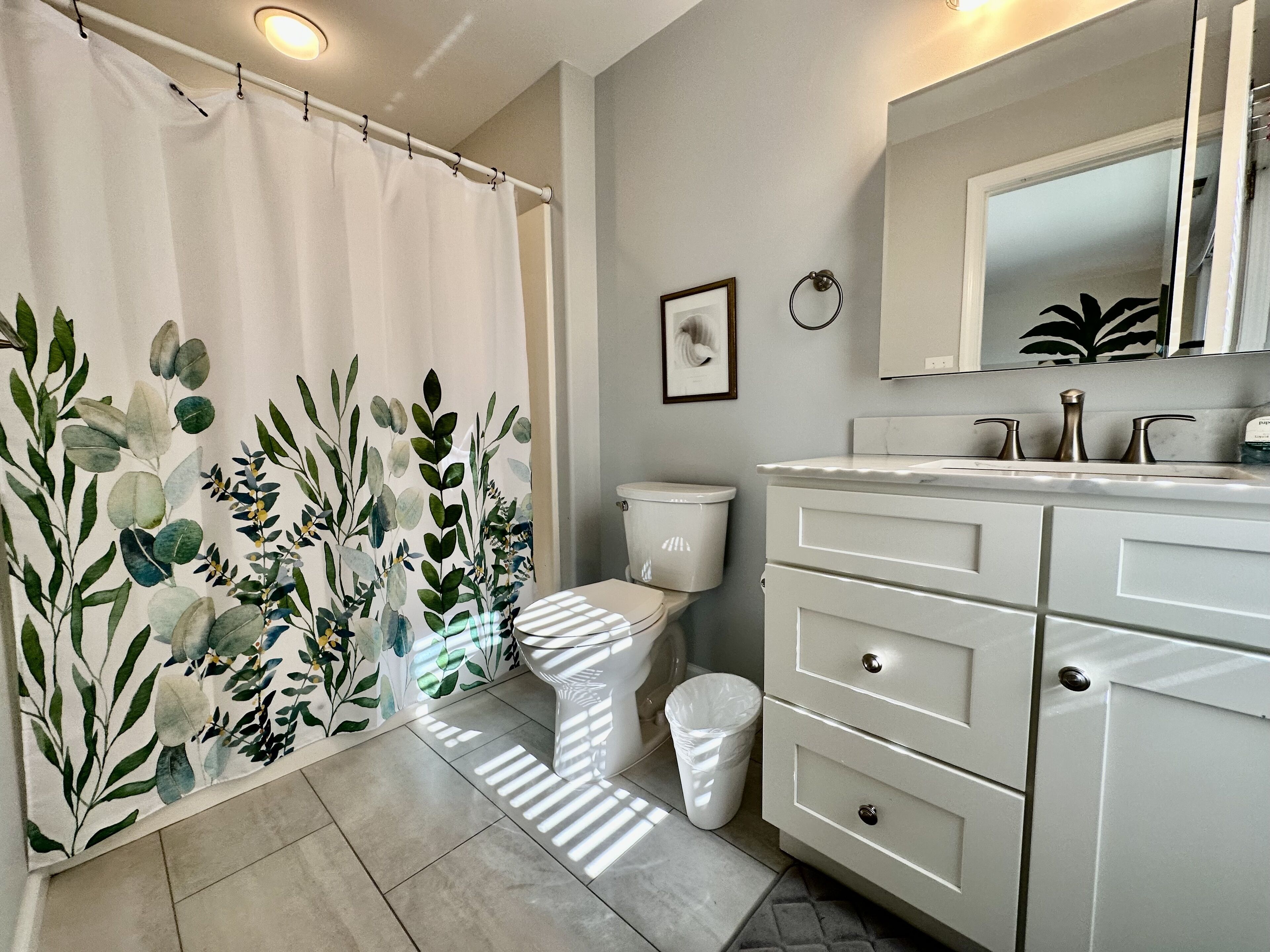 A bathroom with a toilet, a sink with a mirror, and a shower curtain with a leaf pattern.