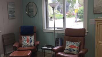 A room with two leather armchairs, a small table, a sofa, and a window with a view of the street.