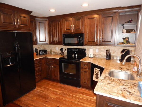 A kitchen with wooden cabinets, a black refrigerator, a microwave, a stove, and a sink.