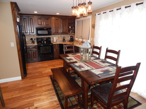 A kitchen with wooden cabinets, a black microwave, and a stove. There is a dining table with chairs and a bench. - Beautiful Rustic Townhome - Lodge Theme (Galena)