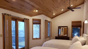 A bedroom with two beds, wooden ceiling, large windows with curtains, a ceiling fan, and a dresser with a mirror. - Lake Superior Home - Perfect for a family vacation any time of the year! (Calumet)