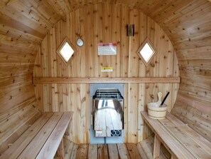 A sauna with wooden walls, a central heater, two benches, and warning signs.