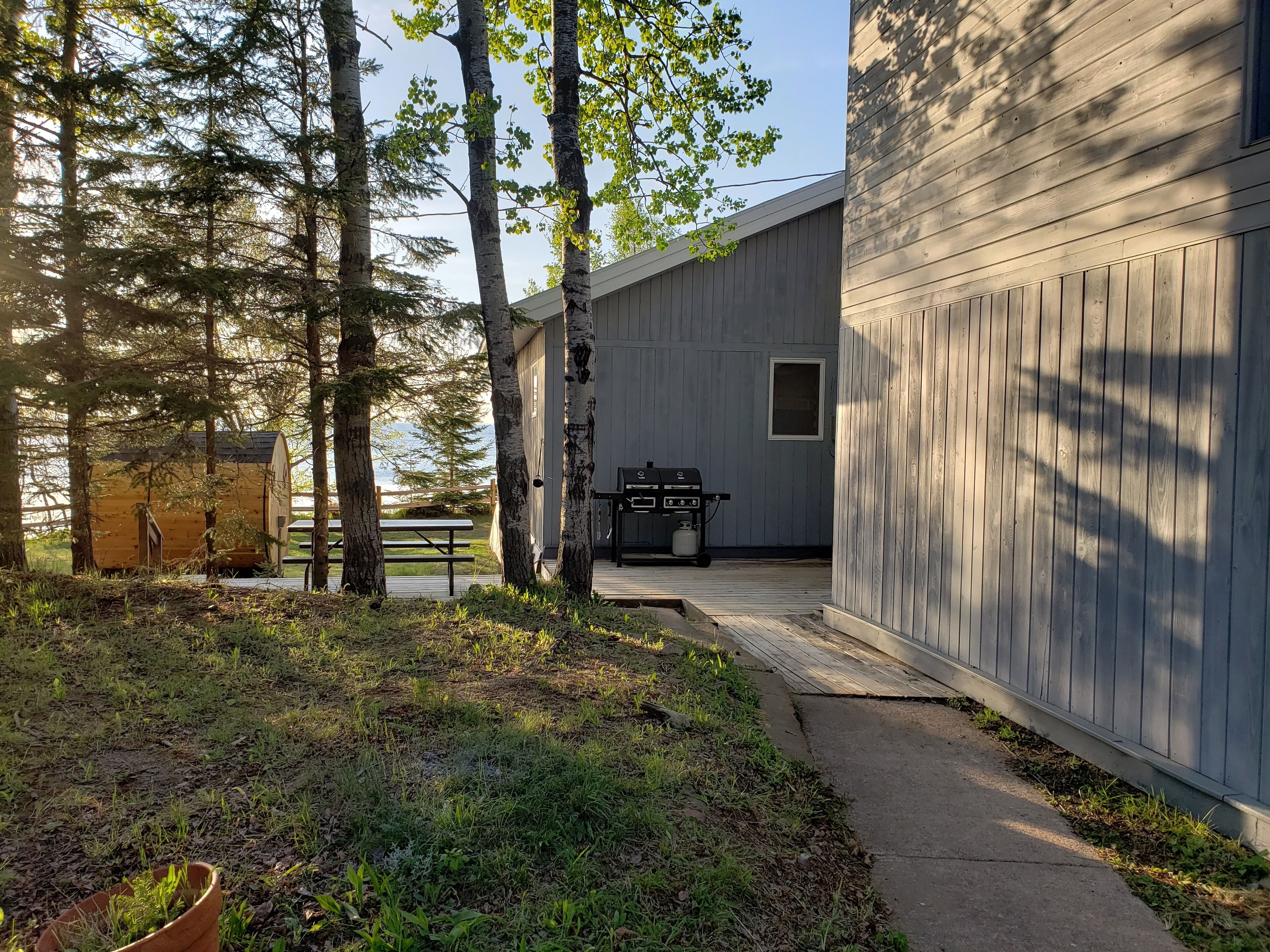 A wooden deck with a barbecue grill, a picnic table, and a small wooden structure.