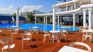 A cruise ship deck with a swimming pool, outdoor seating, and a covered area with tables and chairs.