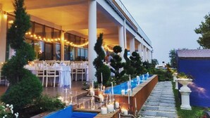 An outdoor dining area with tables set for a meal, surrounded by a pool and a pathway.