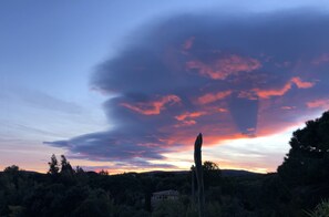 Un coucher de soleil sur un paysage avec une maison et des arbres.
