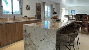 A modern kitchen with a marble island, pendant lighting, and a dining area with wicker chairs. - Contemporary villa 500 m beach and club 55 (Ramatuelle)