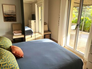 Une chambre à coucher comprenant un lit, une chaise, un bureau et une porte-fenêtre coulissante donnant sur un espace extérieur.