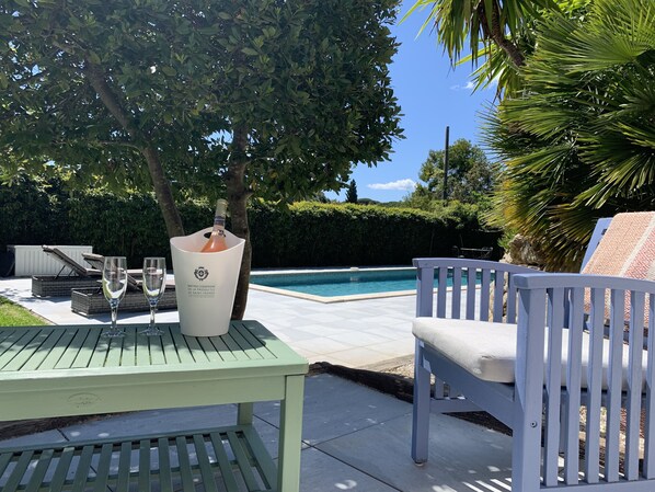 A poolside area with a table, two chairs, and a bottle of wine. - Contemporary villa 500 m beach and club 55 (Ramatuelle)