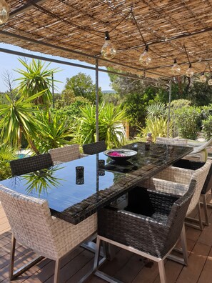 Un espace de restauration en plein air avec une table en verre, des chaises en osier et un toit de chaume.