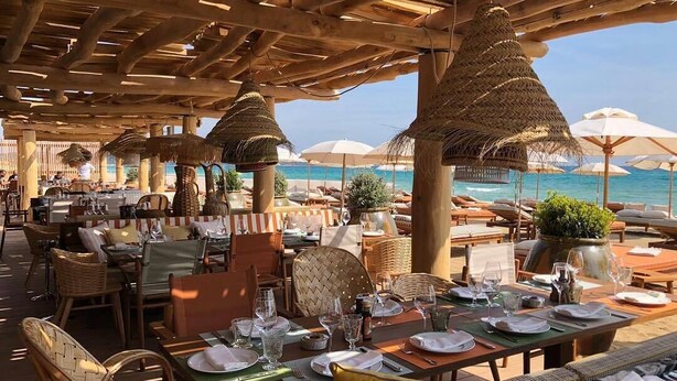 An outdoor dining area with tables set for guests, thatched umbrellas, and a view of the sea. - Contemporary villa 500 m beach and club 55 (Ramatuelle)