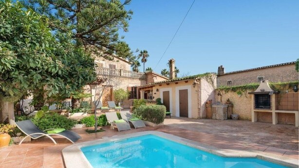 Piscina com espreguiçadeiras, um edifício de pedra e um jardim.
